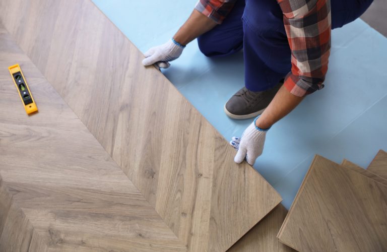 Worker installing laminated wooden floor indoors, closeup